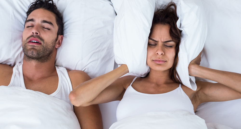 Woman blocking ears while man snoring on bed